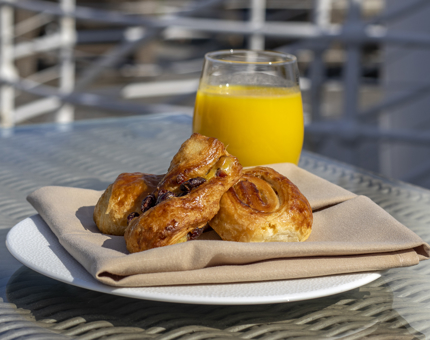 Danish pastries on a plate with a glass of orange juice on a table outside on Fingal's deck.
