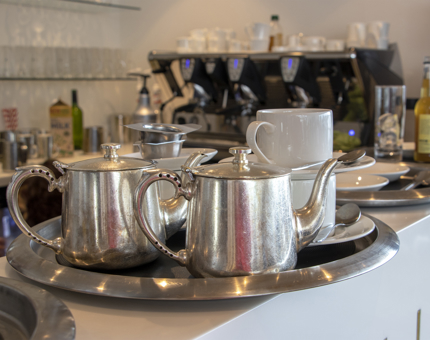 A tray containing two silver teapots, cups and saucers.