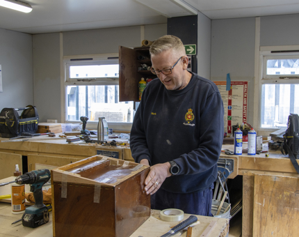 A member of the Maintenance team in the workshop repairing a small storage box. 