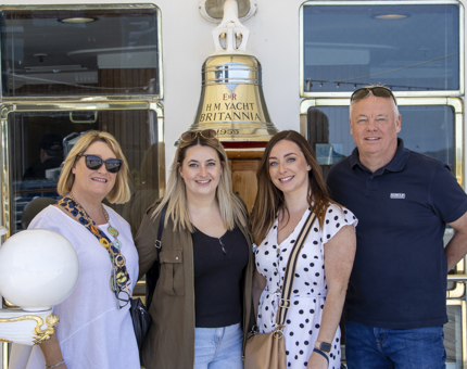 A group of four visitors stand next to Britannia's ship's bell. 