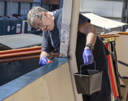 A man painting the edge of the hull at the upper deck. 