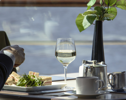 A smoked salmon sandwich and a glass wine on a table in the Royal Deck Tearoom. 