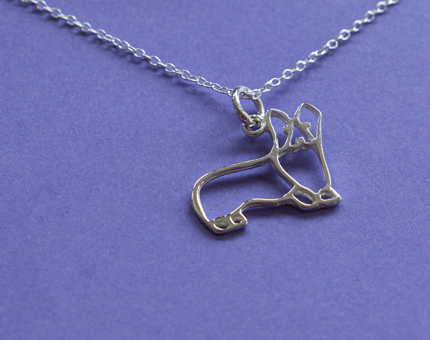 A silver necklace shaped in the outline of a corgi. 