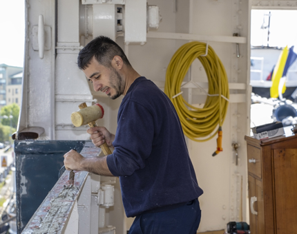 Another view of the Maintenance team member as he is removing the adhesive from a handrail before painting. 