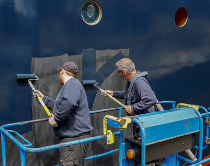 Two men are painting the side of Britannia's hull.