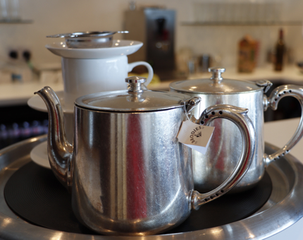 Polished teapots, cups and saucers on a tray in the Tearoom. 
