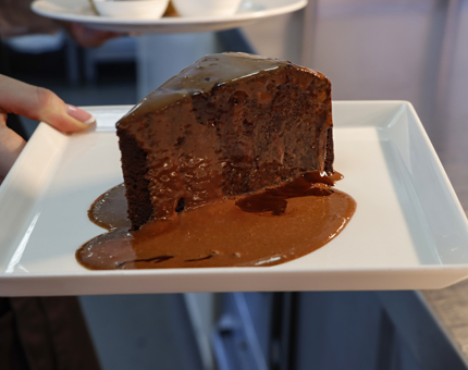 A large slice of chocolate fudge cake sitting on a square plate and ready to be served in the Tearoom. 
