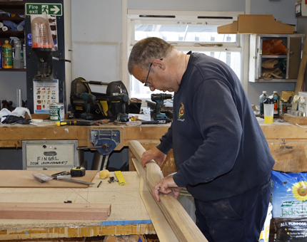 A man working on a wooden handrail in the workshop.