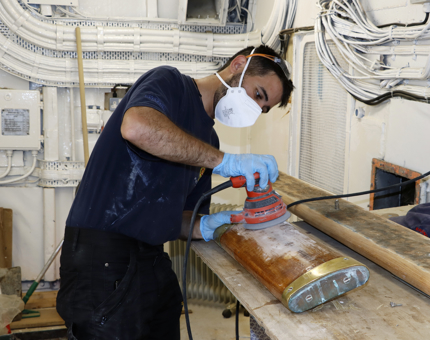 A Maintenance team member sanding a wooden handrail. 
