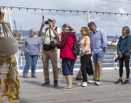Several visitors standing on Britannia's Verandah Deck, admiring the Compass Binnacle. 