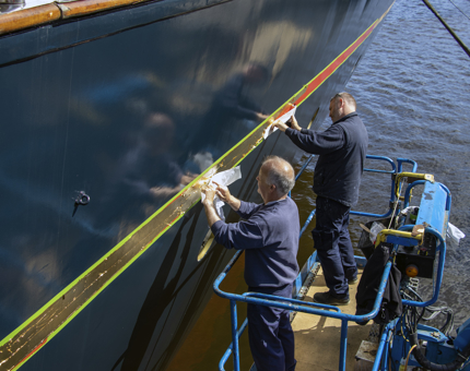 Two men on a cherry picker applying the 24-carat gold leaf for the gold line. 