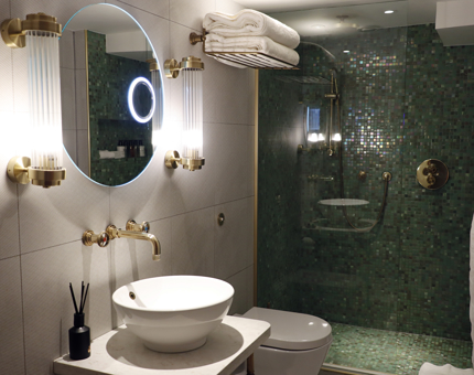 A bathroom within a classic cabin at Fingal containing brass nautical details and a green mosaic tiled shower. 