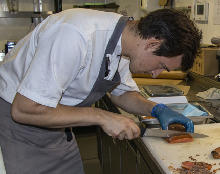 A chef working in the Galley slicing smoked salmon. 