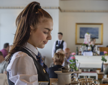 A Waiter carrying a tray containing a teapot, cups and saucers in the Tearoom. 