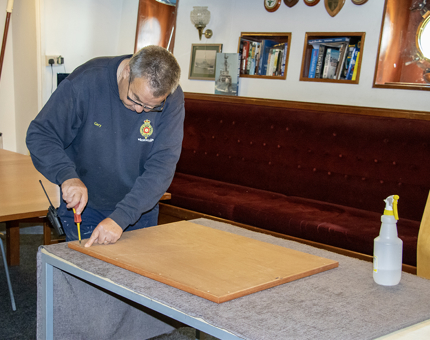 A member of the Maintenance team fitting the back to a wooden picture frame in the workshop. 