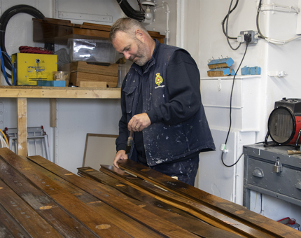A man in the workshop varnishing wooden handrails with a brush.