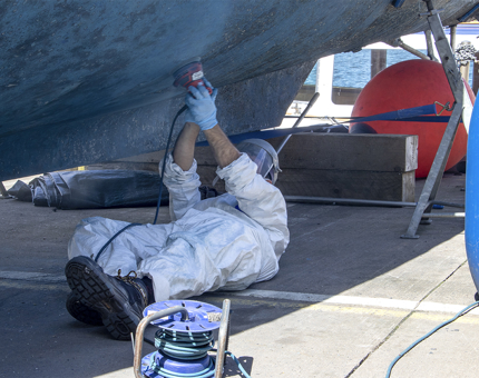 A man lying on the ground sanding the bottom of the hull on the Fast Motor Launch (FML).