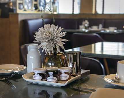 A table set for breakfast in Fingal's Lighthouse Restaurant & Bar with a tray containing jams and marmalade, a vase with a flower and condiments. 
