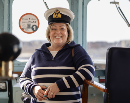 A woman wearing a Captain's hat leaning against the Captain's chair in the Bridge. 