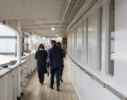 Visitors walking along a sheltered deck listening to their audio guide handset. 