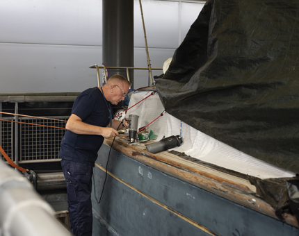 At Britannia's Royal Barge, a man is removing varnish with a heat gun. 