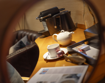 Reflected in a round mirror in a cabin abord Fingal is a coffee maker, teapot and teacup and newspaper.