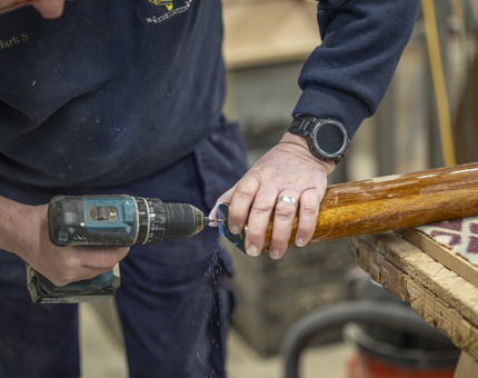 A man holding a power drill, adding brass ends to handrails.