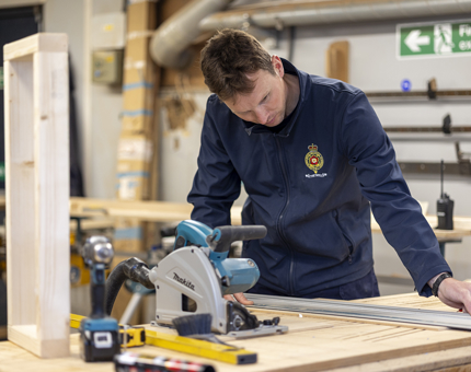 A Maintenance team member measuring wood to make a desk for an onboard office.