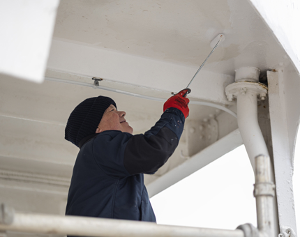 A closer look at a Maintenance team member holding a paint roller, applying a coat of white paint.