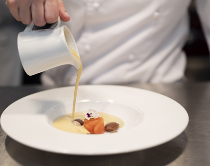 A chef pouring Jerusalem artichoke soup into a white bowl.