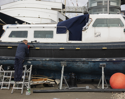 A maintenance team member working to refurbish the Admiral's Fast Motor Launch boat.
