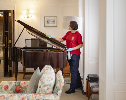 A Housekeeper is polishing the lid of a grand piano in the Drawing Room aboard The Royal Yacht Britannia in Leith.