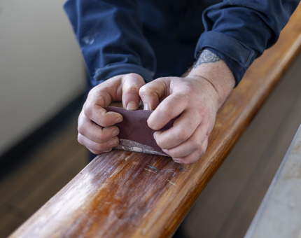 A close up of hands sanding a handrail.