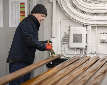 A Maintenance team member holding a paint brush varnishing handrails.