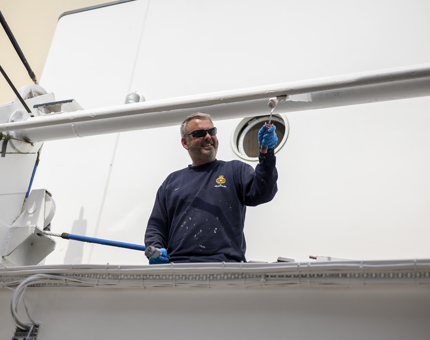 A maintenance man is applying a coat of white paint to the port side of the Yacht.