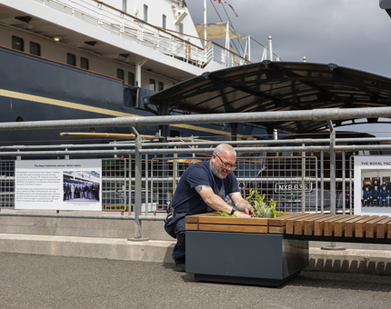 A Facilities Officer is on the Quayside planting herbs in a planter. 