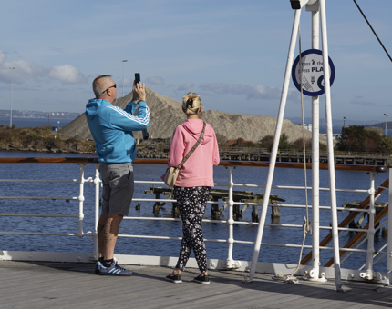 A man and a woman on the Verandah Deck taking a photo of the port of Leith.