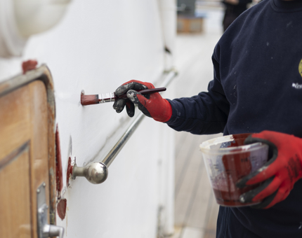 A close look at a hand holding a paintbrush and pot of paint. Applying a coat of primer to the wall.