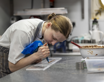 A chef is holding a blue piping bag full of chocolate, creating bunny ears. 