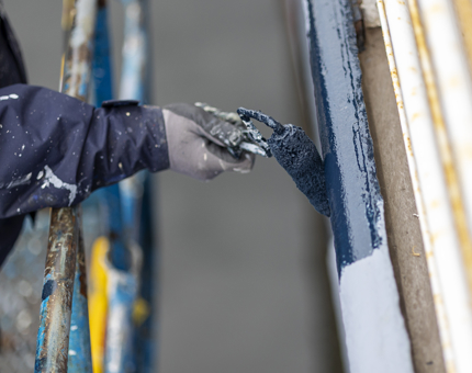 A close up of a hand holding a paint roller, painting the side of Fingal blue.