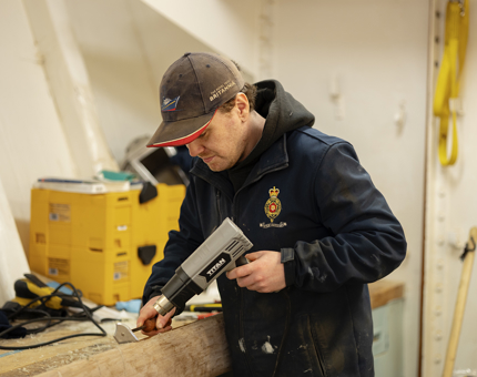 A an holding a heat gun over a handrail to remove varnish. 
