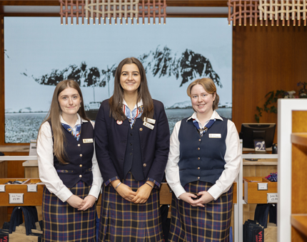 Three female members of the Retail team pose for a photo in front of the Shop's tills. 
