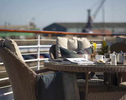A table and chairs on the deck of Fingal. There is an open book with a teapot and cup next to it.