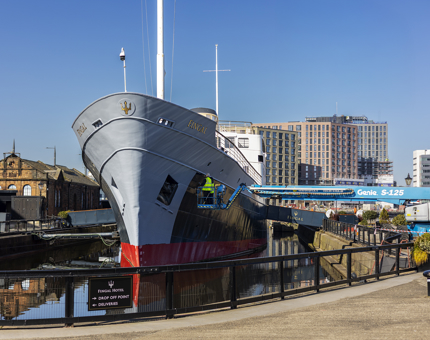 On a cherry picker, two Maintenance team members are painting the ship, Fingal.