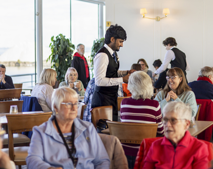 Visitors sitting at tables in the Royal Deck Tearoom. There are servers taking orders. 