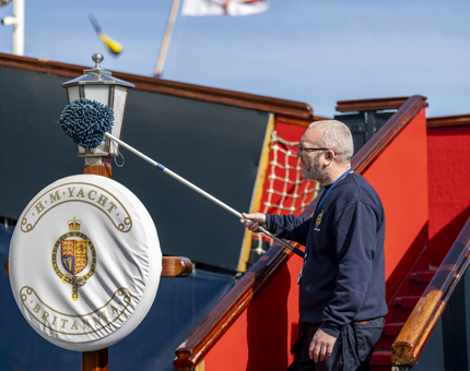 Facilities Officer, Billy, is standing on the Royal Brow holding a duster, he is cleaning the lamp above a perry buoy.