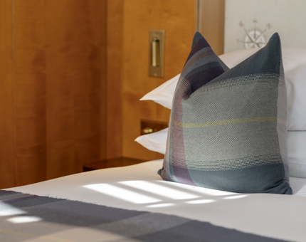 A close up of a bed aboard Fingal Hotel. It has white sheets and pillows, there is also a tartan throw pillow and blanket.