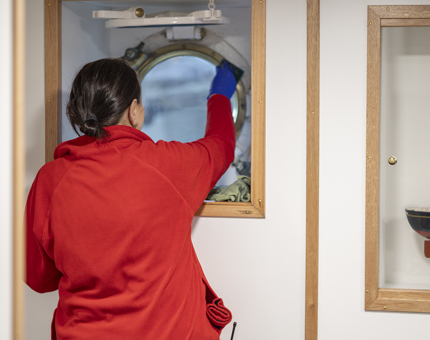 A member of the Housekeeping team cleaning a round window.