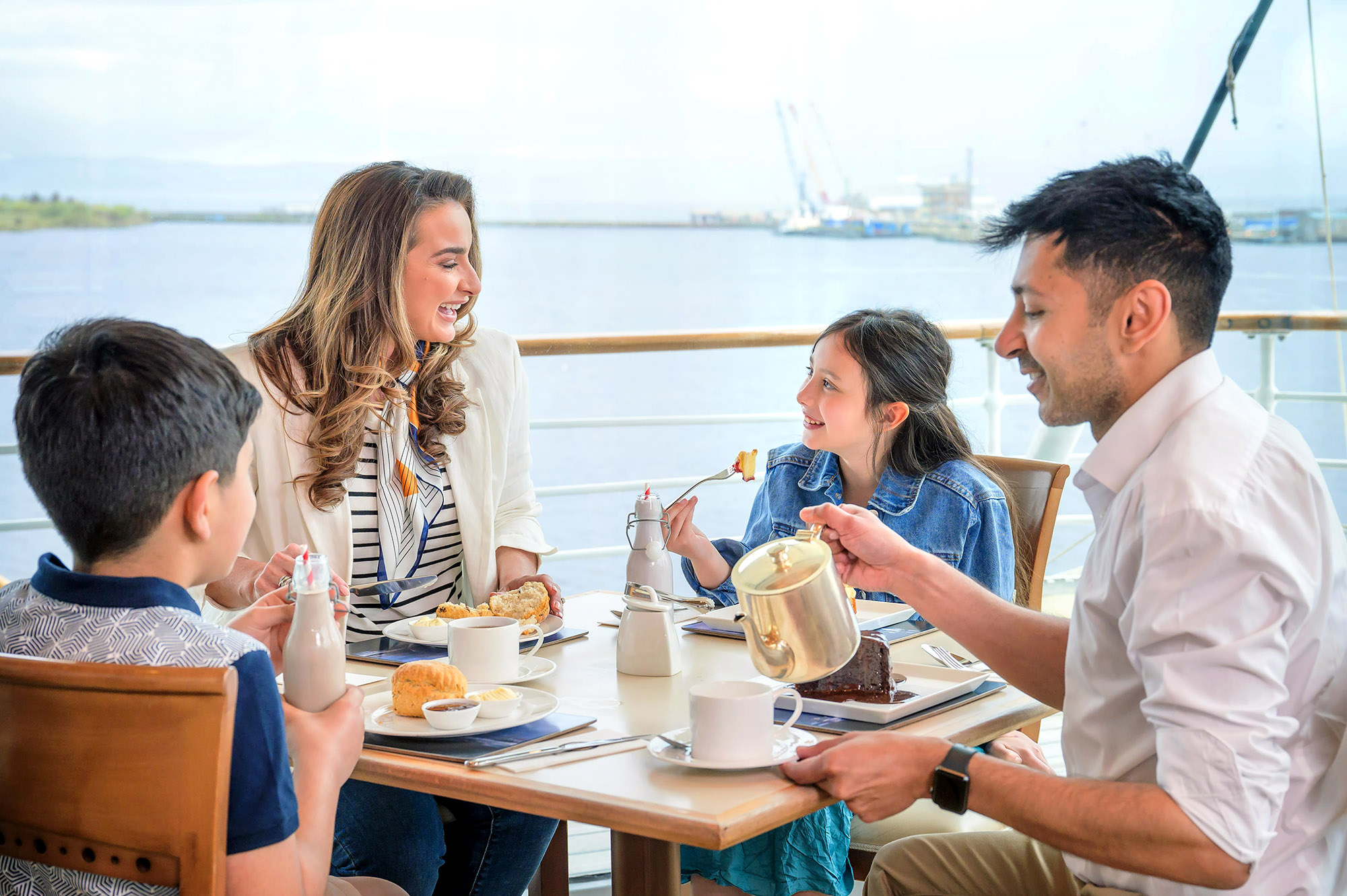 A family sitting at a table in the Royal Deck Tearoom in Edinburgh. The Port of Leith can be seen behind them.