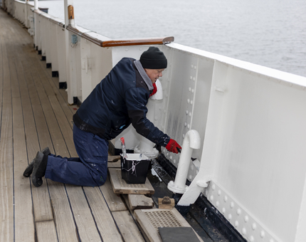 Kneeling on the ground is a Maintenance man who is painting the sides of the walkway white.